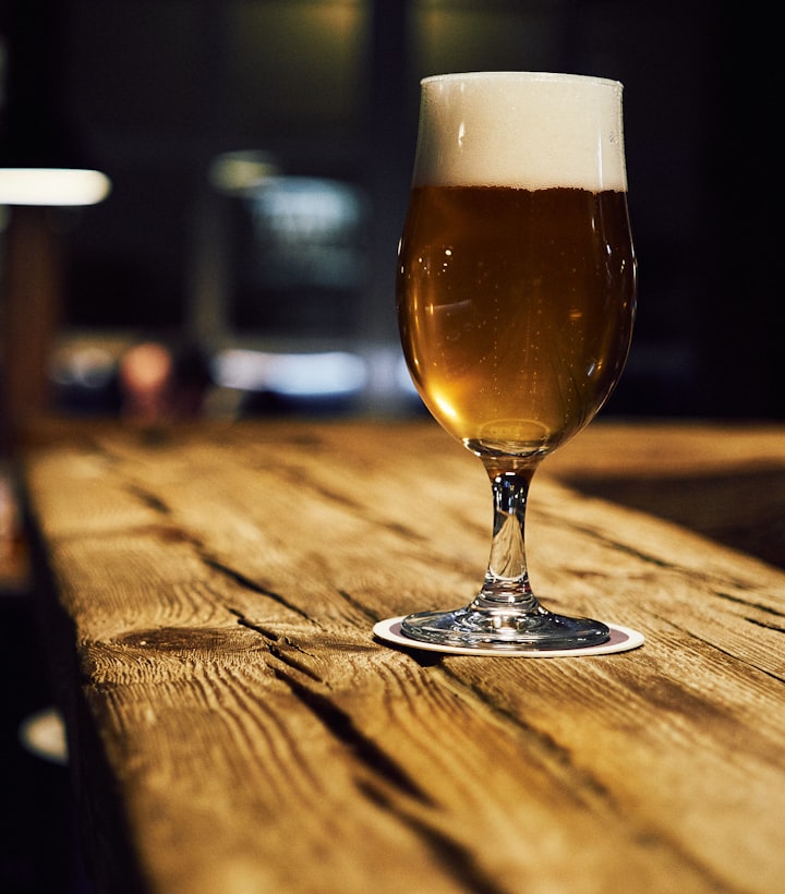 Head brewer inspecting a glass of beer beside towering copper brew kettles
